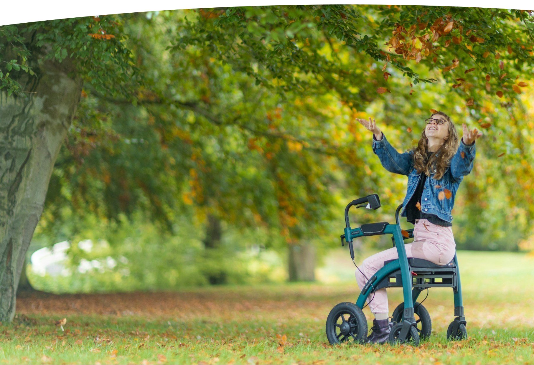 Female person smiling and sitting on a rolling walker in a park throws leaves into the air